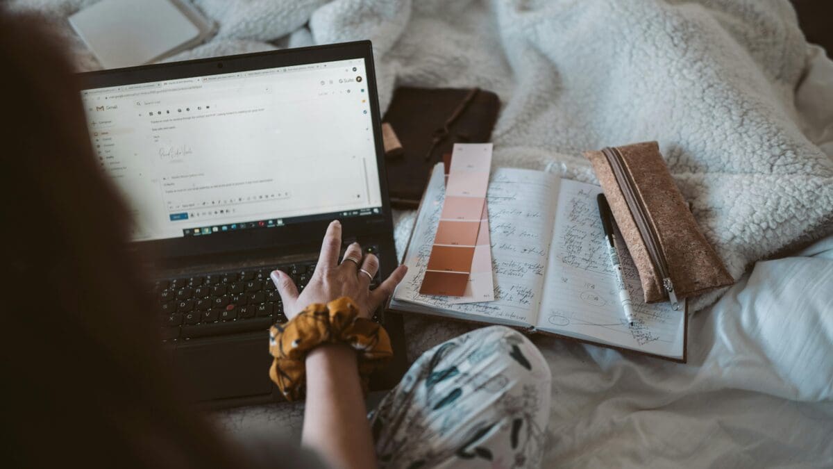 a shoulder view of a woman working on a laptop, with makeup swatches next to her on top of a notebook