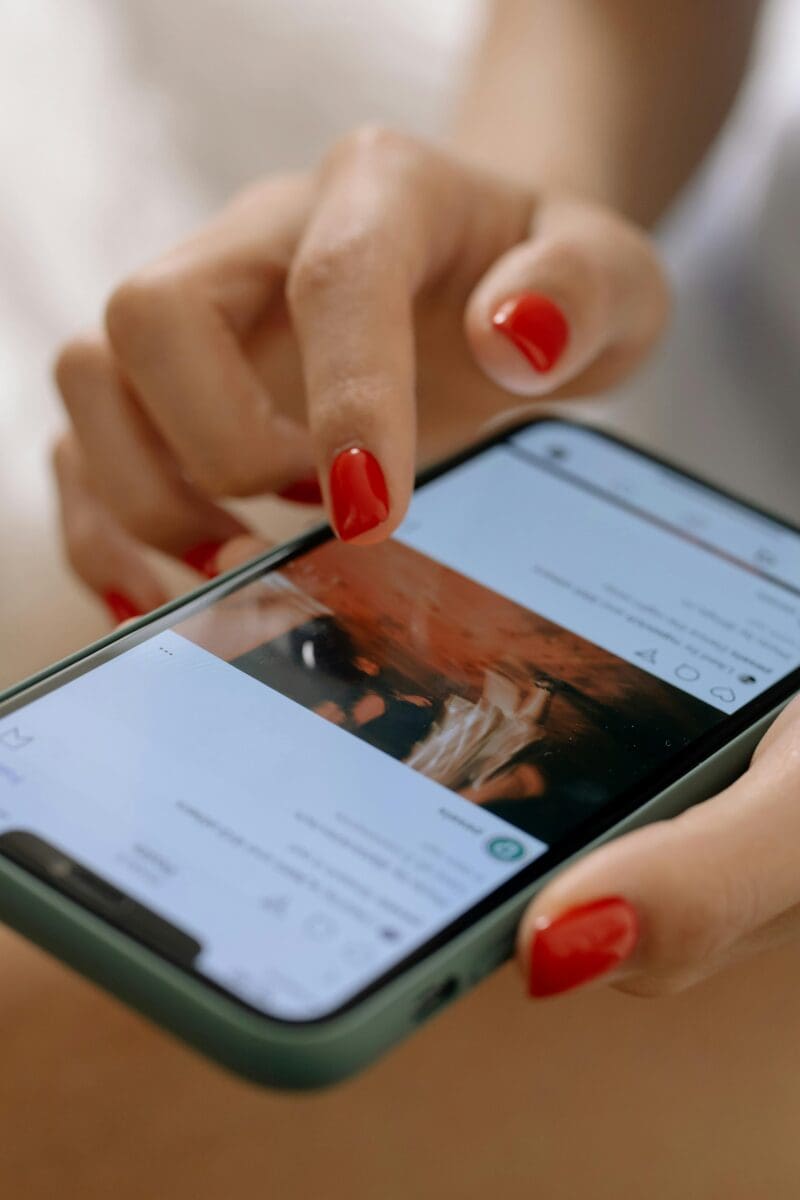 Close-up of a person with red nail polish using a smartphone to scroll through a social media post.