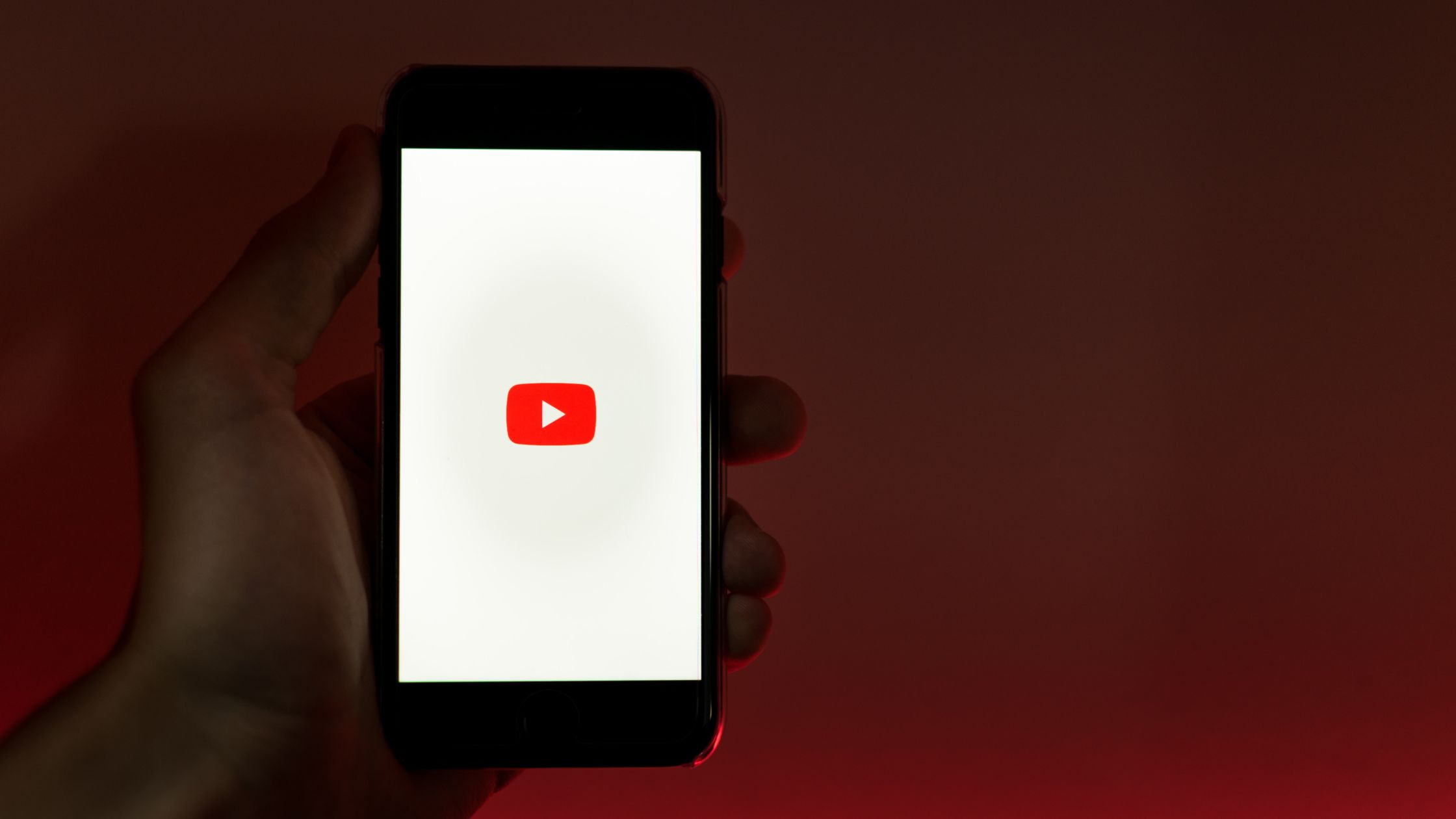 A hand holds a smartphone showing the YouTube logo on a white loading screen.